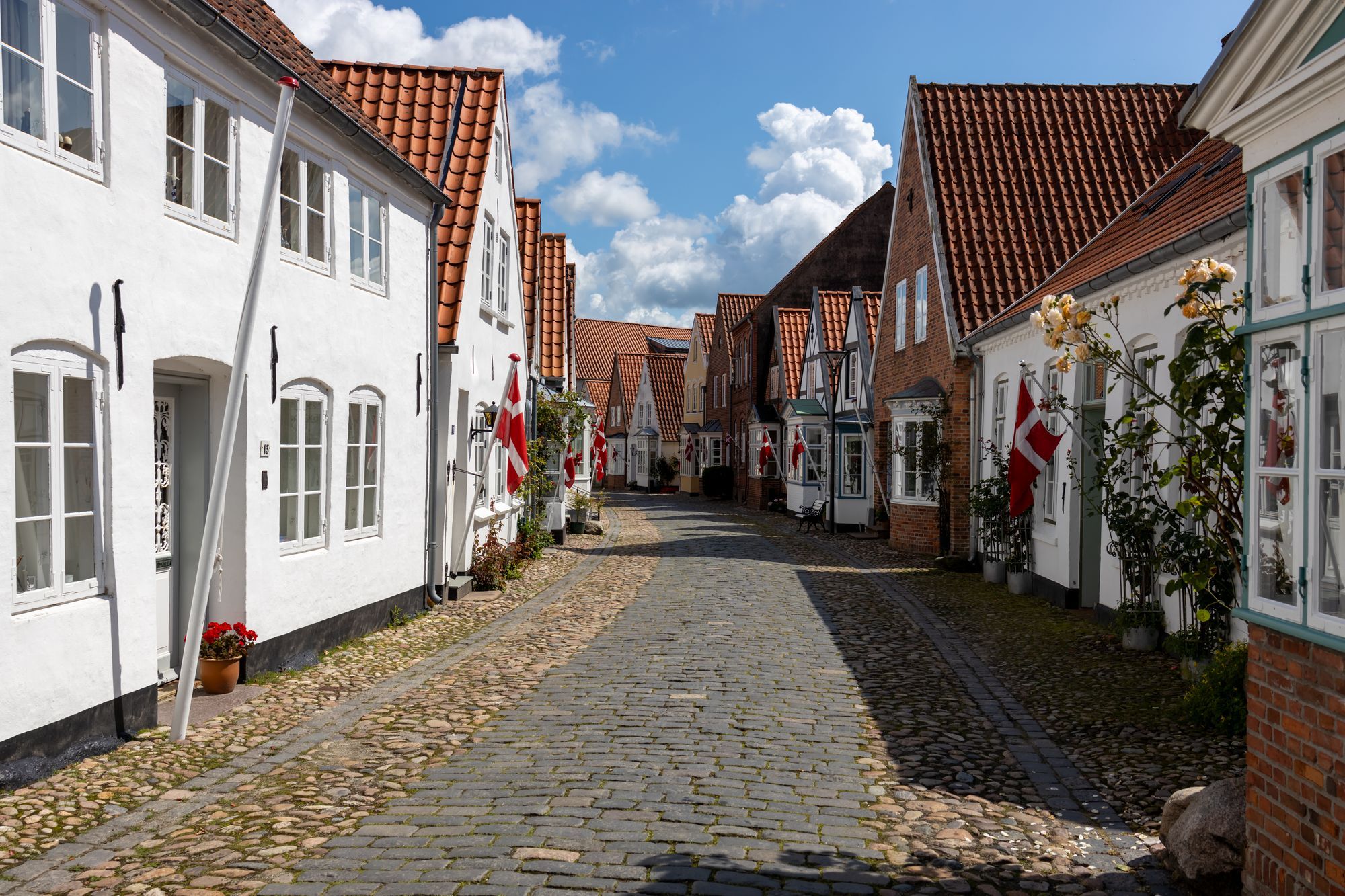 Brostensbelagt gade med hvide huse og røde tage i en dansk by